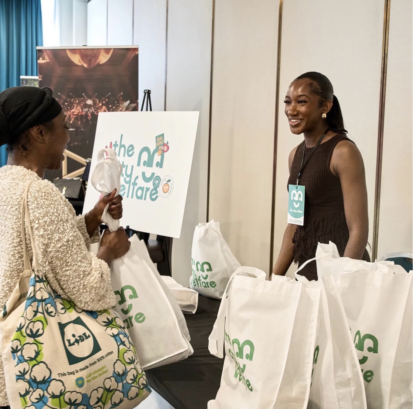 A volunteer greeting a guest with City Welfare branded bags at a community event