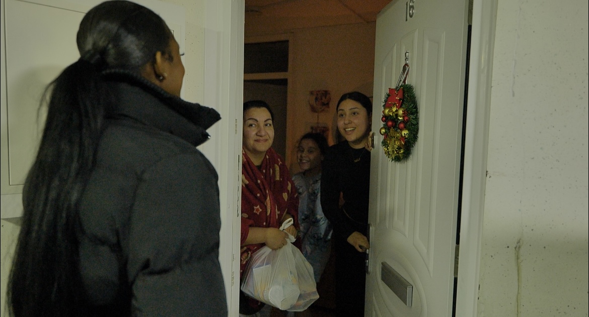 A volunteer delivering groceries to a family welcoming her at their front door