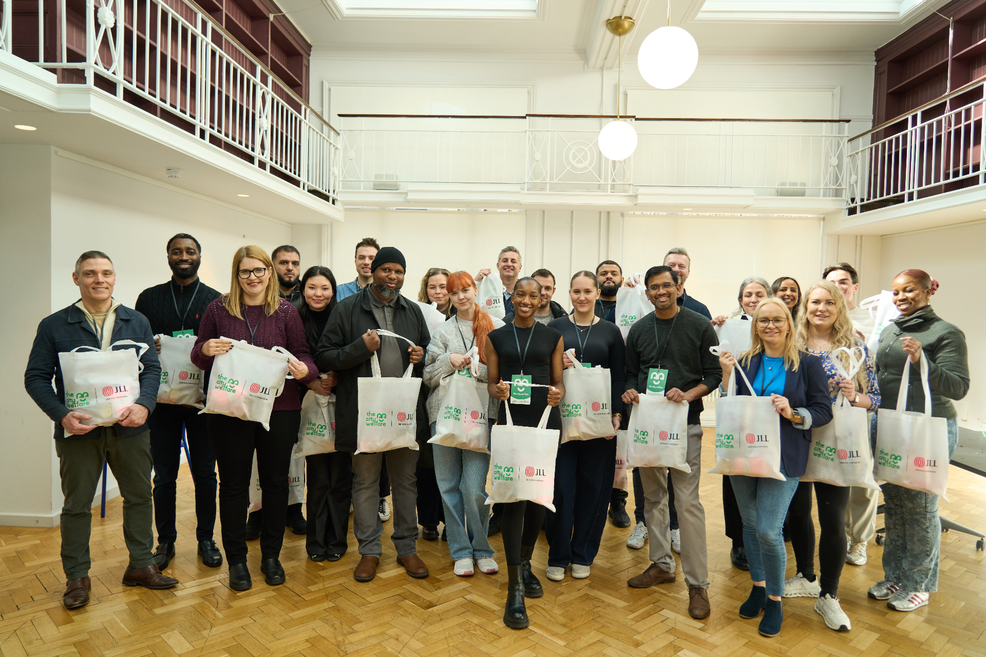 A large corporate volunteering group holding City Welfare branded tote bags after a packing session